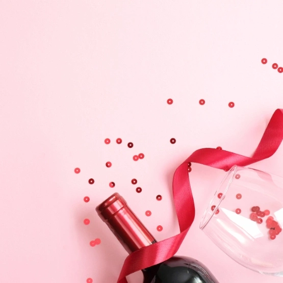 Wein, Glas, Band und Konfetti auf rosa Hintergrund. Romantisch.