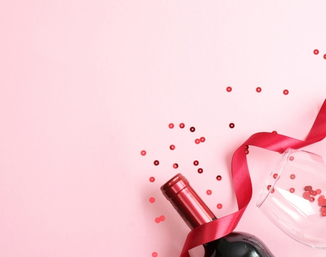 Wein, Glas und rotes Band auf rosa Hintergrund mit Konfetti