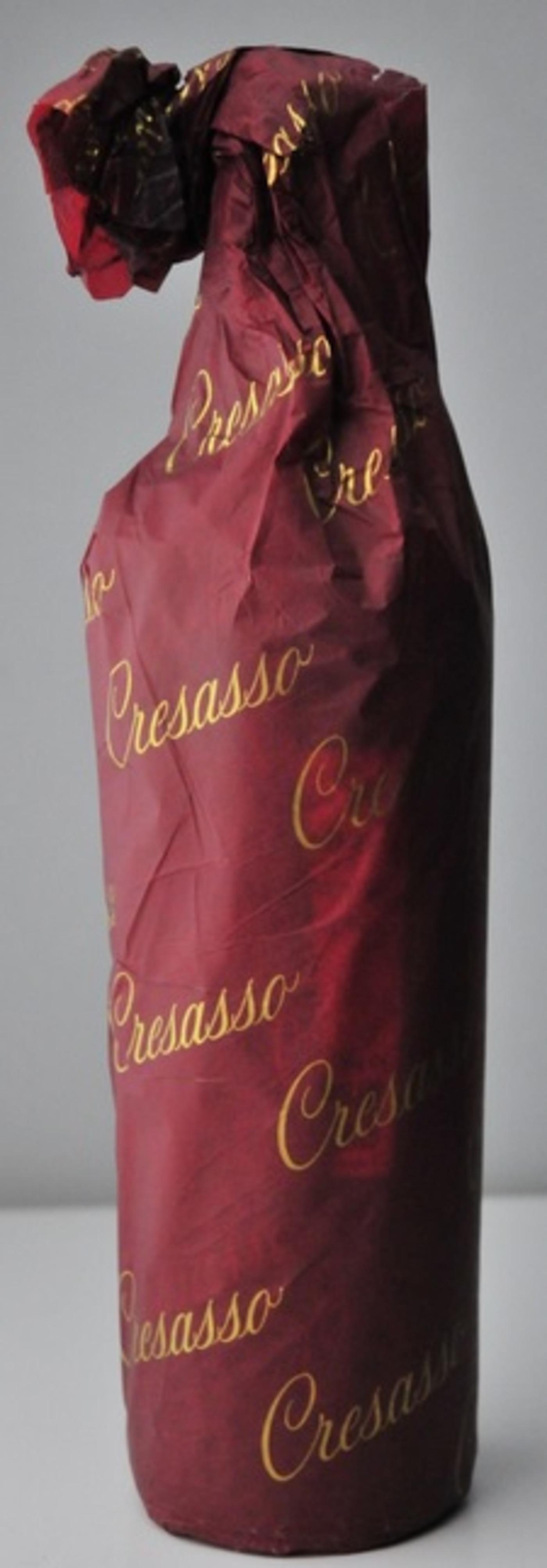 Eine Weinflasche in rotem Papier mit goldener Aufschrift Cresasso verpackt.