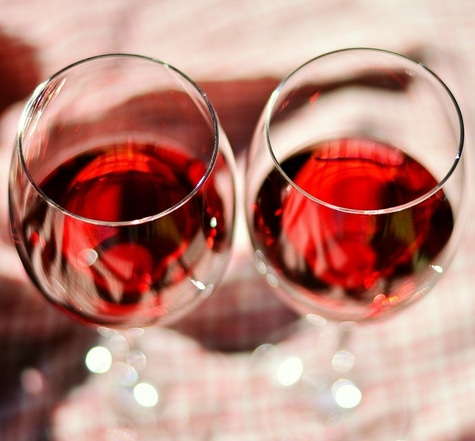 Zwei Weingläser mit Rotwein, die auf einem karierten Tischtuch stehen.